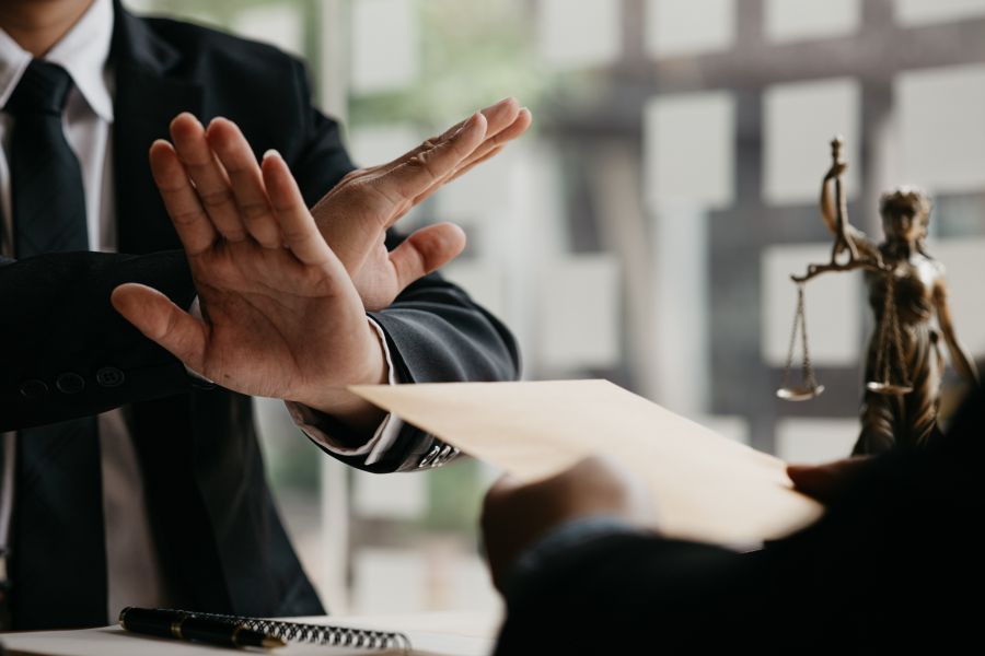 a man in a suit waves his hands no with Lady Justice statue in the background